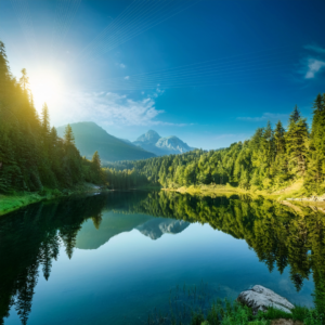 Lake with trees around the banks of the crystal blue water - sun shining in the background - peaceful setting
